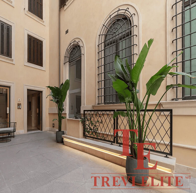 Изысканный внутренний дворит с зелеными растениями и красивыми окнами в стиле классической архитектуры. Идеальное место для отдыха или встреч в элегантной атмосфере.