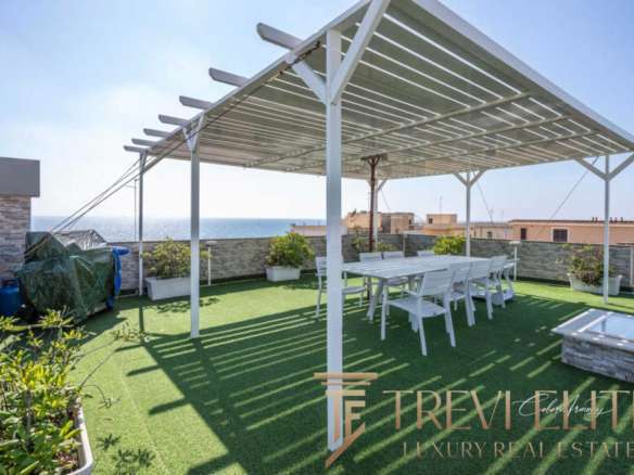 Уютная терраса с солнечной защитой, цветущими растениями и видом на море, идеально подходит для отдыха и приёма гостей на роскошной недвижимости в Италии.