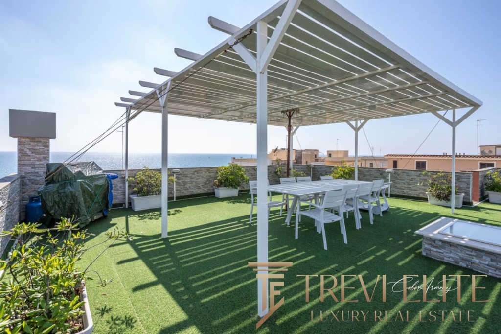 Уютная терраса с солнечной защитой, цветущими растениями и видом на море, идеально подходит для отдыха и приёма гостей на роскошной недвижимости в Италии.