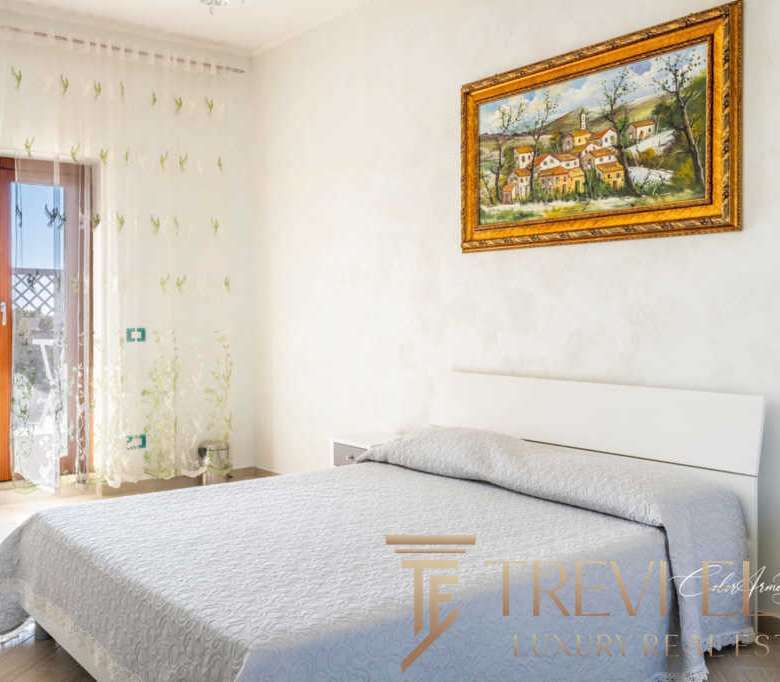 Роскошная спальня с видом на балкон и уютной атмосферой, элегантное оформление, светлые оттенки, современная мебель, картины в золотых рамах, множество солнечного света, подходящая для высококлассной недвижимости.