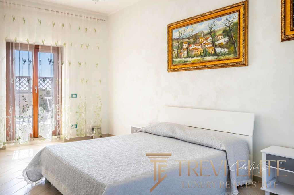 Роскошная спальня с видом на балкон и уютной атмосферой, элегантное оформление, светлые оттенки, современная мебель, картины в золотых рамах, множество солнечного света, подходящая для высококлассной недвижимости.