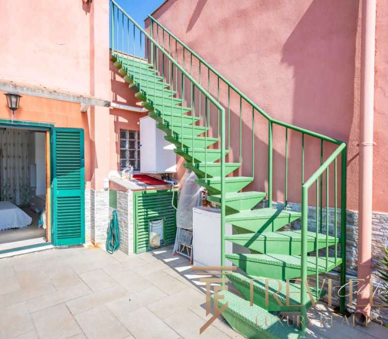 Кастомный зеленый наружный лестничный пролет на зеленой лестнице с чередующимися ступеньками и перилами, ведущий к верхним этажам роскошного здания в стиле итальянского курорта.