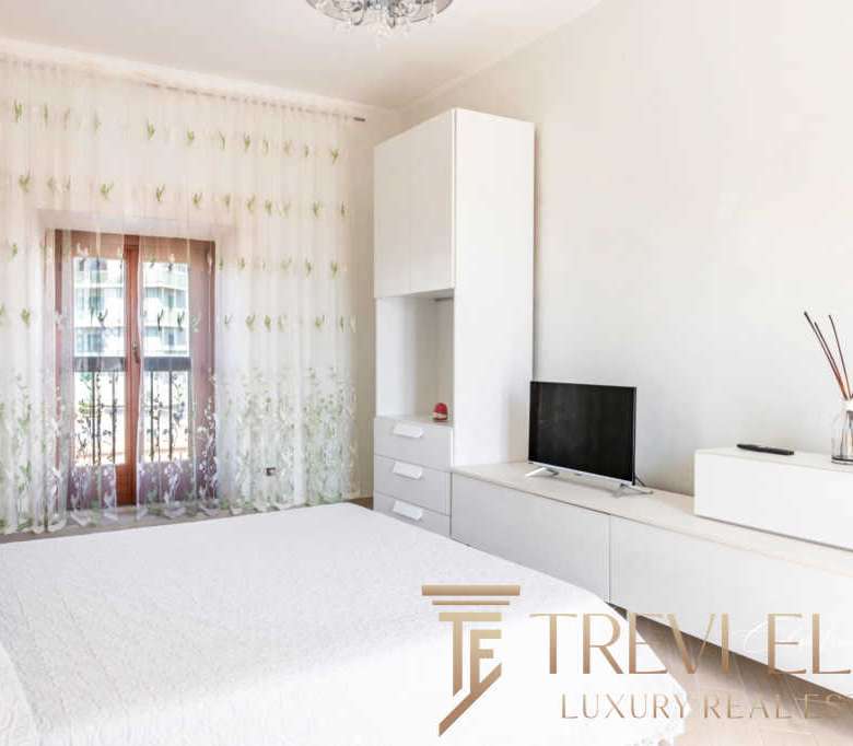 Элитная спальня с мягким светом, белой мебелью и современными деталями, привлекающая внимание к высокому уровню роскоши и комфорта в недвижимости Треви Элит.