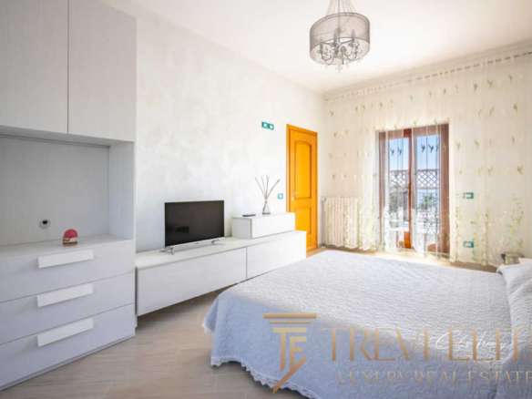 Роскошная спальня с чистым дизайном и уютной атмосферой, большие окна с шторками и французским балконом, светлый интерьер, современные элементы, подходящая для элитной недвижимости.