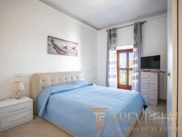 Уютная спальня с большой кроватью, светлыми стенами и видом на балкон. Современный интерьер, свежие ткани и простор создают комфорт и роскошь для жильцов.