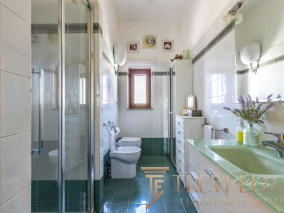 Окно ванной комнаты с зеркальным шкафом, зеленой раковиной и ванной, украшенной цветами, в светлом пространстве с современным дизайном и естественным освещением.