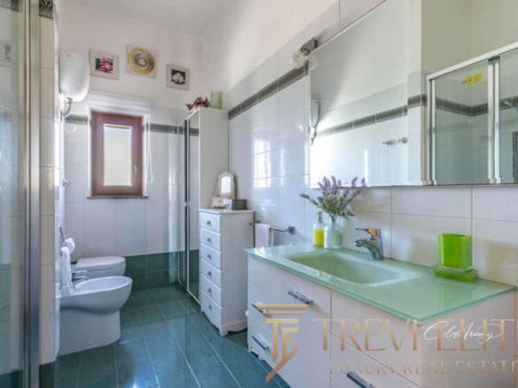 Современная ванная комната с белыми стенами и зеленым акцентным умывальником, большое зеркало и аккуратная мебель, создающие атмосферу уюта и роскоши в престижной недвижимости.