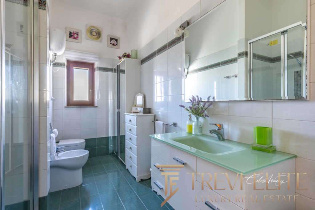 Современная ванная комната с белыми стенами и зеленым акцентным умывальником, большое зеркало и аккуратная мебель, создающие атмосферу уюта и роскоши в престижной недвижимости.