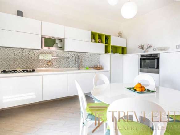 Современная светлая кухня с белыми шкафами и зелеными акцентами в интерьере, стильное пространство для комфортной жизни в элитной недвижимости.