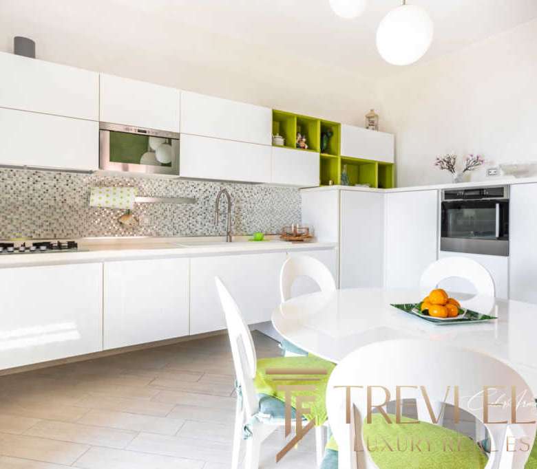 Современная светлая кухня с белыми шкафами и зелеными акцентами в интерьере, стильное пространство для комфортной жизни в элитной недвижимости.