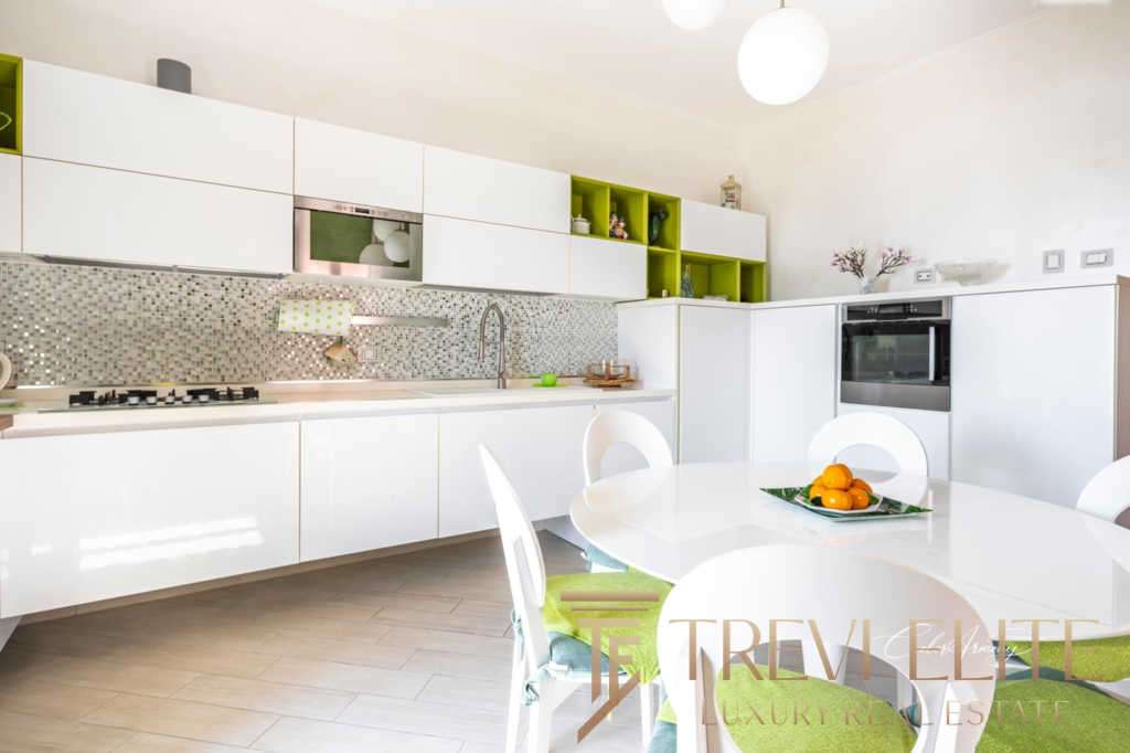 Современная светлая кухня с белыми шкафами и зелеными акцентами в интерьере, стильное пространство для комфортной жизни в элитной недвижимости.