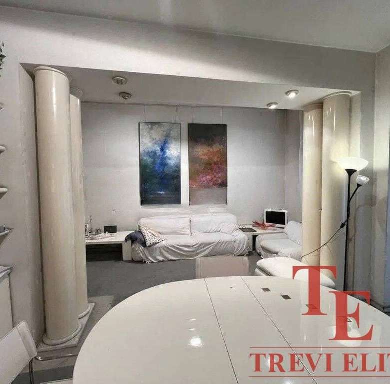 Элегантная гостиная в роскошной недвижимости от агентства Треви Элит, с уютным диваном, современной техникой и стильным интерьером, идеально подходит для комфортного отдыха и приема гостей.