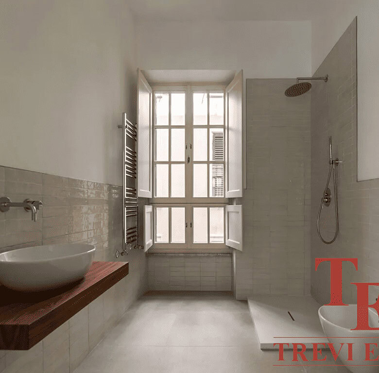 Современная уютная ванная комната с большой тепловой лампой и стильной раковиной на деревянной полке под большое окно, создающие светлую и комфортную атмосферу.