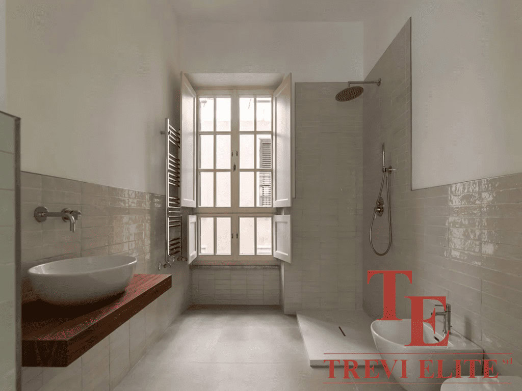 Современная уютная ванная комната с большой тепловой лампой и стильной раковиной на деревянной полке под большое окно, создающие светлую и комфортную атмосферу.