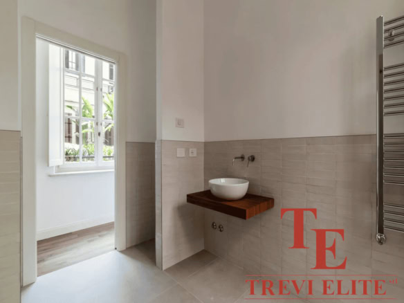 Уютная ванная комната с современным дизайнерским решением, умывальник на деревянной полке и яркое естественное освещение из окна. Идеальный интерьер для роскошной недвижимости.