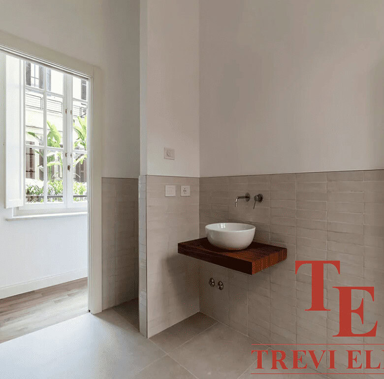 Уютная ванная комната с современным дизайнерским решением, умывальник на деревянной полке и яркое естественное освещение из окна. Идеальный интерьер для роскошной недвижимости.