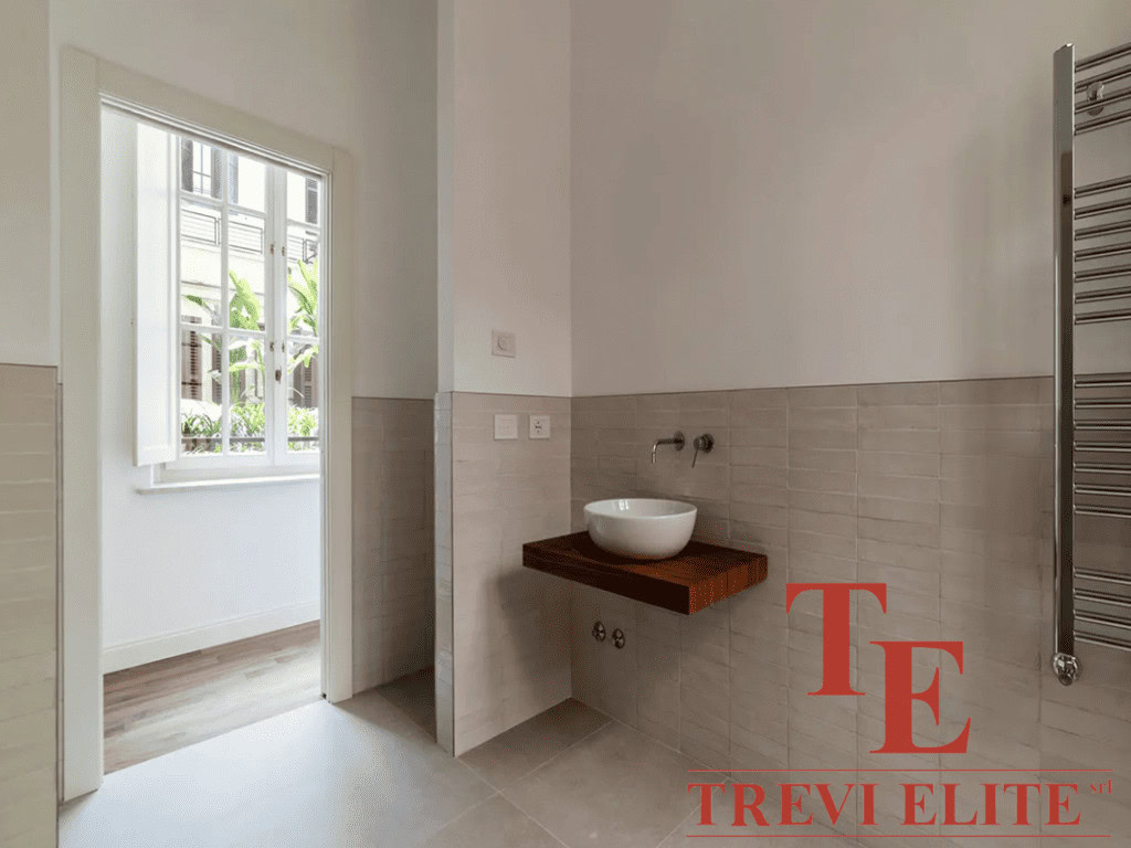 Уютная ванная комната с современным дизайнерским решением, умывальник на деревянной полке и яркое естественное освещение из окна. Идеальный интерьер для роскошной недвижимости.