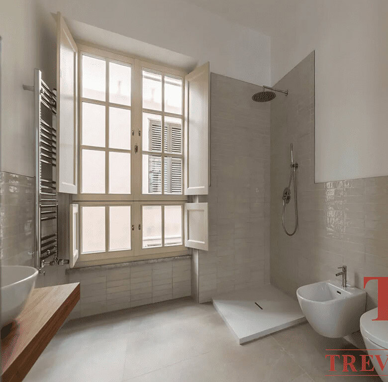 Современный дизайнерский санузел с большой природной подсветкой, окна с деревянными рамами и качественной отделкой. Ванная комната в элитной недвижимости с стильной мебелью и отделочными материалами.