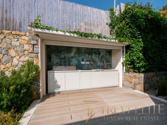 Современная уличная кухня с мозаичной стеной и зеленым садом на заднем дворе. Идеальное место для отдыха и приготовления пищи на свежем воздухе в роскошной недвижимости.