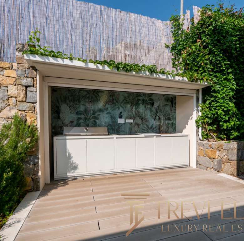 Современная уличная кухня с мозаичной стеной и зеленым садом на заднем дворе. Идеальное место для отдыха и приготовления пищи на свежем воздухе в роскошной недвижимости.