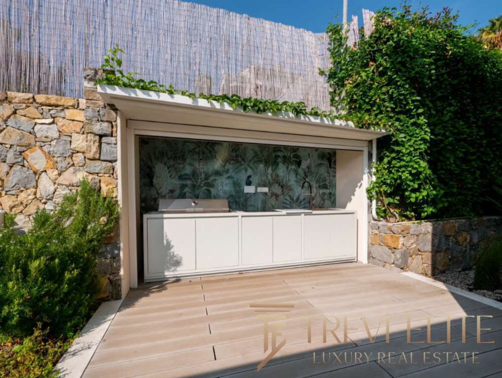 Современная уличная кухня с мозаичной стеной и зеленым садом на заднем дворе. Идеальное место для отдыха и приготовления пищи на свежем воздухе в роскошной недвижимости.