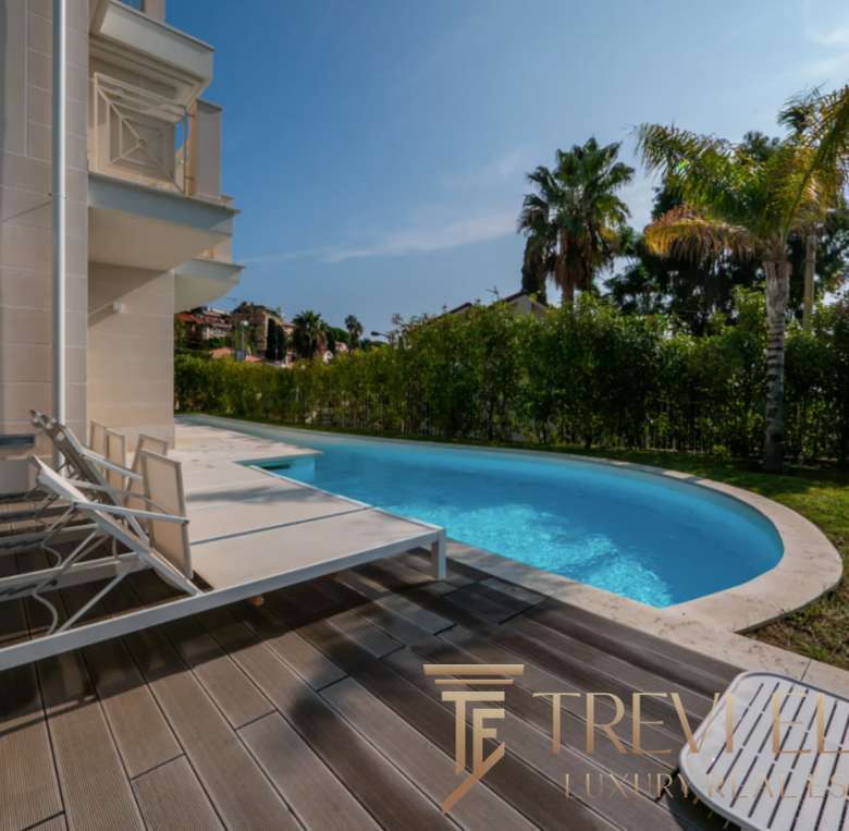 Элитная частная резиденция с изогнутым бассейном и зоной отдыха на террасе, окруженная пальмами и зеленью, стильное оформление недвижимости для роскошного образа жизни.