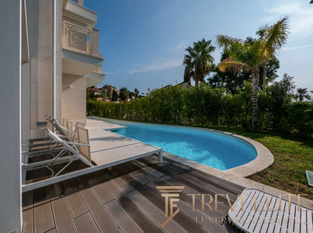 Элитная частная резиденция с изогнутым бассейном и зоной отдыха на террасе, окруженная пальмами и зеленью, стильное оформление недвижимости для роскошного образа жизни.