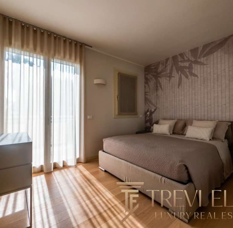 Роскошная спальня в элитной недвижимости, светлый интерьер с видом на окно и стильным дизайном стен, создающая атмосферу уюта и комфорта для высококлассного жилья.