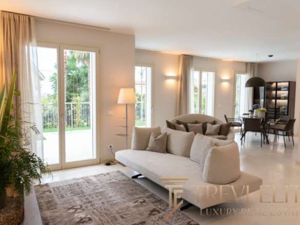 Элитная гостиная с панорамными окнами, современным дизайном, уютной обстановкой и видом на зеленый сад, идеально для отдыха и встреч.