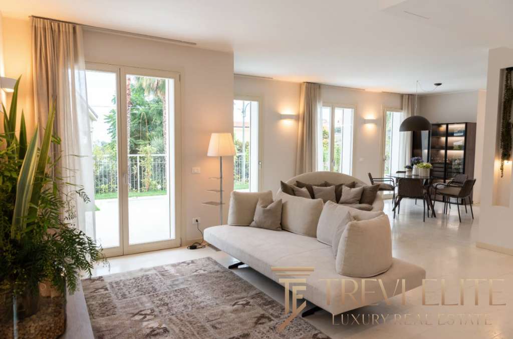 Элитная гостиная с панорамными окнами, современным дизайном, уютной обстановкой и видом на зеленый сад, идеально для отдыха и встреч.