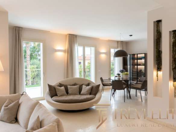 Современная роскошная гостиная с большим уютным диваном, мягкими подушками, просторными окнами и стильной обеденной зоной, идеально подходящая для элитной жизни.