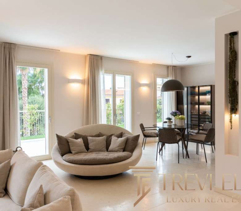 Современная роскошная гостиная с большим уютным диваном, мягкими подушками, просторными окнами и стильной обеденной зоной, идеально подходящая для элитной жизни.