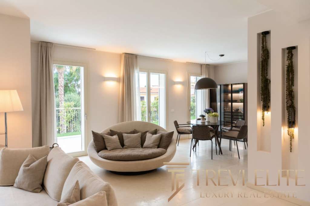 Современная роскошная гостиная с большим уютным диваном, мягкими подушками, просторными окнами и стильной обеденной зоной, идеально подходящая для элитной жизни.