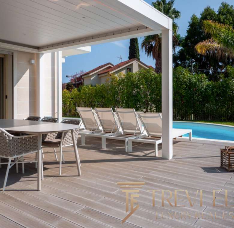 Роскошная терраса с бассейном и шезлонгами, окруженная зеленью и пальмами, идеально подходит для отдыха и развлечений в элитной недвижимости.