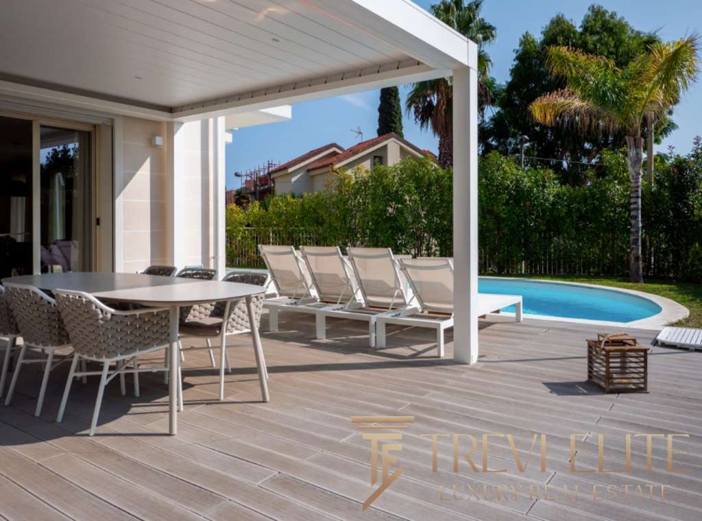 Роскошная терраса с бассейном и шезлонгами, окруженная зеленью и пальмами, идеально подходит для отдыха и развлечений в элитной недвижимости.