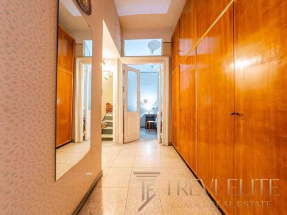 Входная зона квартиры с деревянными шкафами и зеркалом, уютный коридор, ведущий в гостиную и спальню, элегантный интерьер, создающий атмосферу роскоши и комфорта.