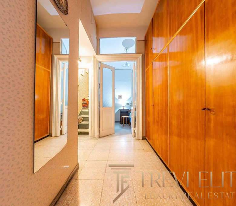 Входная зона квартиры с деревянными шкафами и зеркалом, уютный коридор, ведущий в гостиную и спальню, элегантный интерьер, создающий атмосферу роскоши и комфорта.