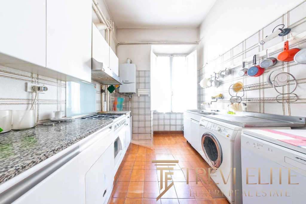 Богатая кухня в уютной квартире с белыми шкафами и стиральной машиной, яркие чашки и посуда в современном стиле, просторное освещенное помещение с окнами и теплым полом.