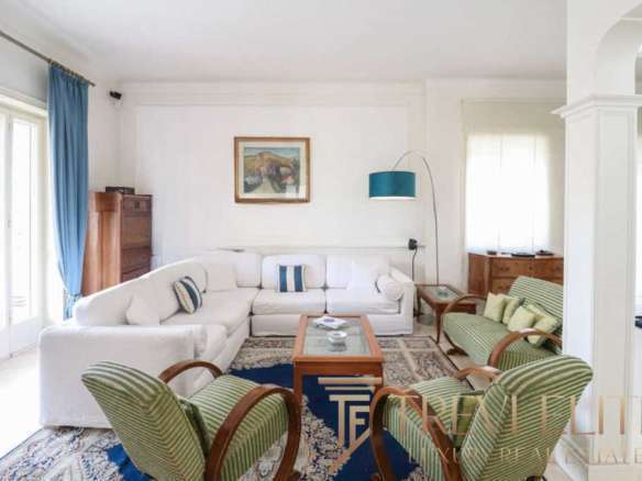 Просторная гостиная в роскошном доме с белой мебелью, зелеными креслами и уютными элементами интерьера, оформленными в светлых тонах, создает атмосферу уюта и элегантности.