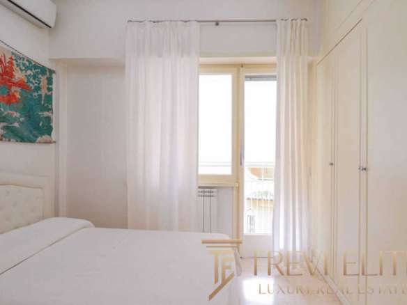 Роскошная спальня с белыми стенами и большими окнами, украшенными светлыми шторами, светлое мебельное оформление, создающее комфортную атмосферу для высококлассной недвижимости.