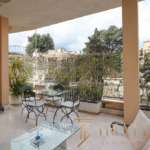 Элегантный балкон с уютной мебелью и зеленью, панорамный вид на город, идеальное место для отдыха и развлечений в роскошной недвижимости.