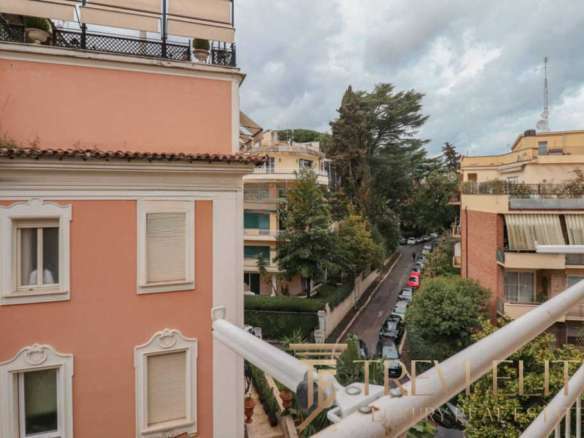 Элегантный вид на жилой район с уютными многоэтажками, зеленью и городской уличной жизнью, идеально передающий атмосферу приватности и престижности элитной недвижимости в Италии.