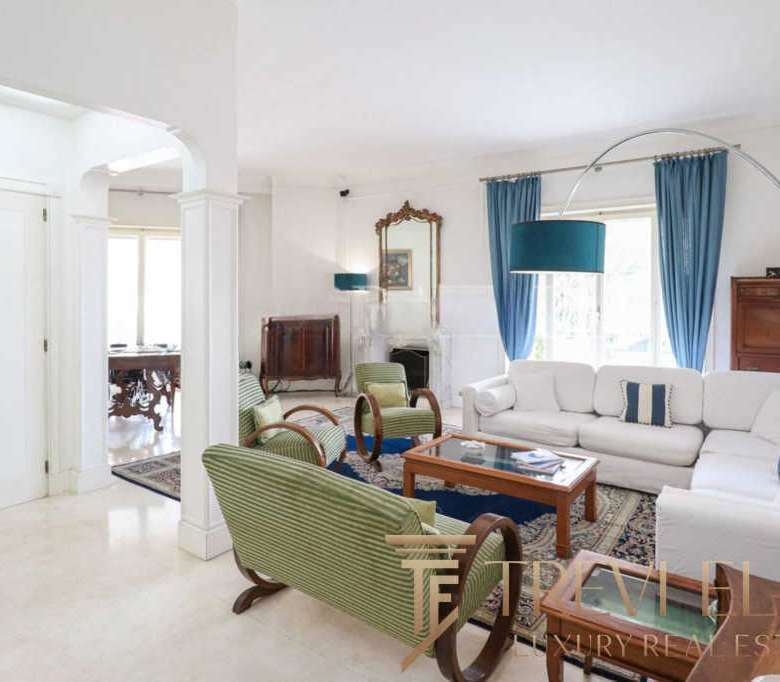 Роскошная гостиная в элитной недвижимости с современным интерьером, яркими голубыми шторами и уютными диванами, подчеркивающая эксклюзивность и высокое качество жилья.