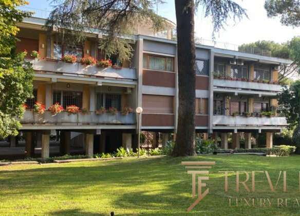Элитный жилой дом на фоне зеленого сада с деревьями и ухоженной территорией, демонстрирующий роскошную недвижимость в премиум-классе для клиентов Trevi Elite.