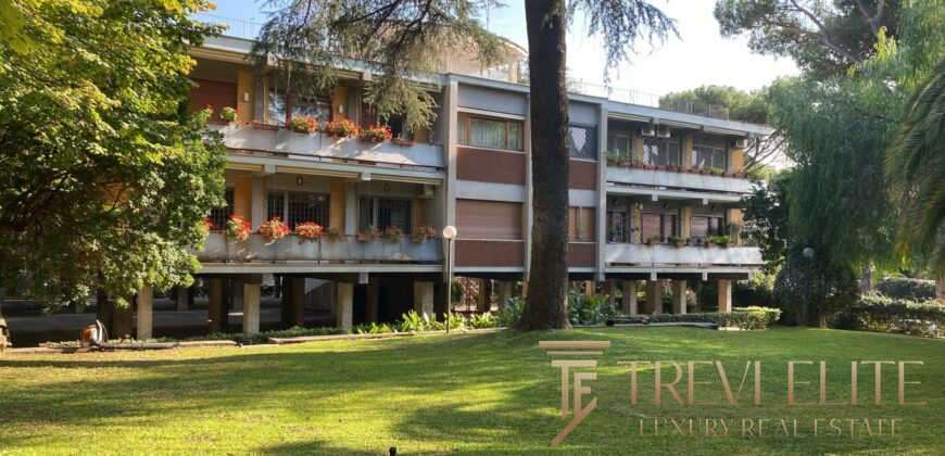 Элитный жилой дом на фоне зеленого сада с деревьями и ухоженной территорией, демонстрирующий роскошную недвижимость в премиум-классе для клиентов Trevi Elite.