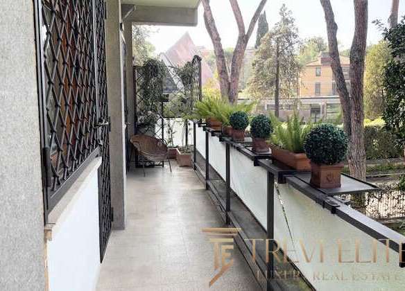 Элегантный балкон с зелеными растениями и видом на зелень и здания в окружении, прекрасное место для отдыха и наслаждения природой.