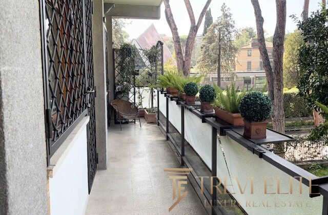 Элегантный балкон с зелеными растениями и видом на зелень и здания в окружении, прекрасное место для отдыха и наслаждения природой.