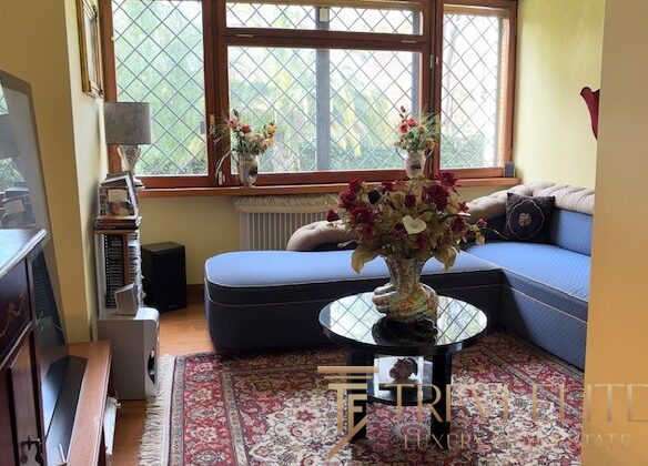 Уютная гостиная с большим окном, мягким диваном и цветочной композиции на журнальном столике, создающая теплую атмосферу уюта и стиля в элитной недвижимости.