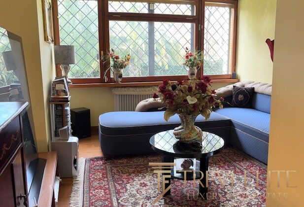 Уютная гостиная с большим окном, мягким диваном и цветочной композиции на журнальном столике, создающая теплую атмосферу уюта и стиля в элитной недвижимости.