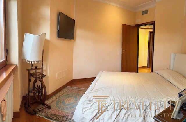 Уютная спальня с мягкой кроватью, телевизором и классическим украшением в стиле антика, светлые стены, панорамное окно, создающее теплую атмосферу для комфортного отдыха.